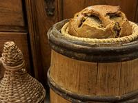 Brot im Brotkorb auf Weinfass, links daneben steht ein gewebtes Gefäß zur Weinflaschenaufbewahrung