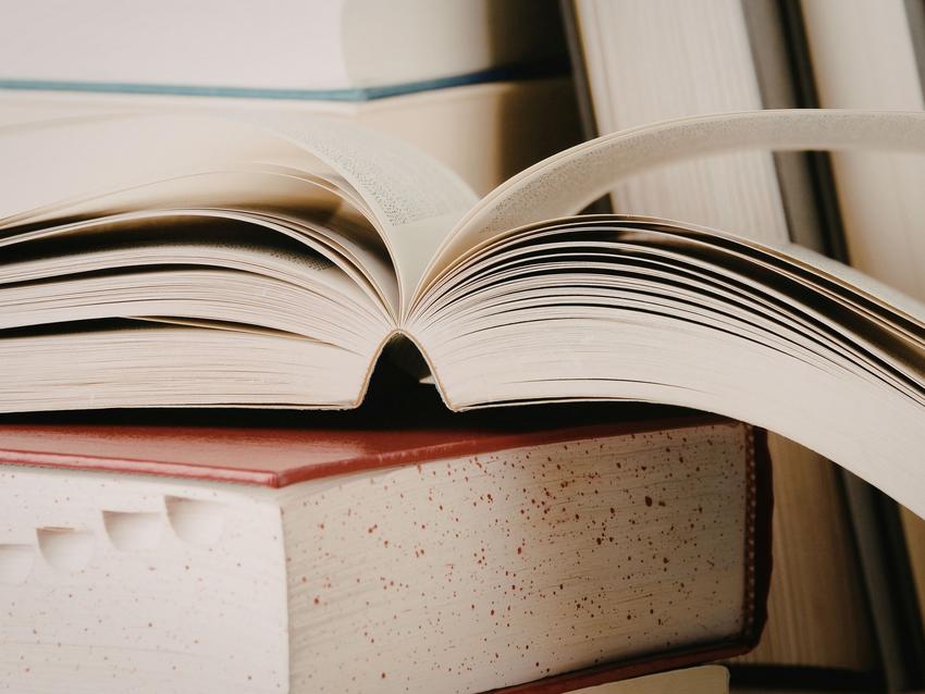 diverse Bücher im Hntergrund - geöffnetes Buch liegt auf geschlossenem