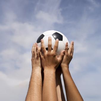 Erhobene Hände halten einen Fußball hoch