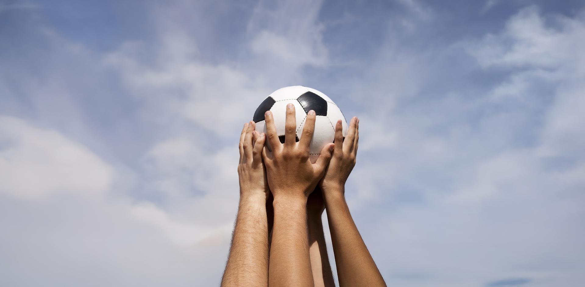 Erhobene Hände halten einen Fußball hoch