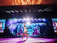 Andrea Berg in Glitzerkleid und Highheels auf einer Bühne mit Feuerwerk im Hintergrund.