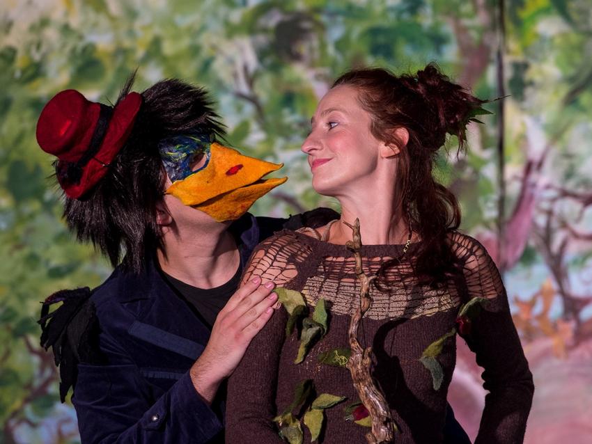 Auf dem Foto sind zwei Schauspieler abgebildet, die sich ansehen. Eine ist als Hexe verkleidet, die andere ein Vogel.